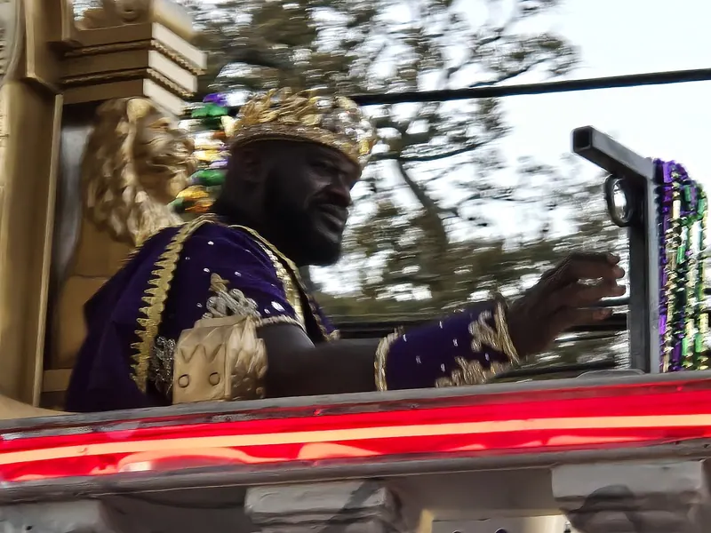 Shaquille O'Neal, crowned and robed in purple and gold as the 2025 Krewe of Bacchus celebrity monarch, waves from his throne float during the Mardi Gras parade in New Orleans.